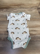 Top-down view of newborn white Kyte Baby short-sleeve bodysuit with hedgehog print and mint trim on wood background size 0-3m