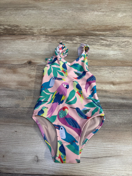 Flat lay of pink TEA girls one-piece swimsuit with colorful bird print and ruffle shoulder on wood background