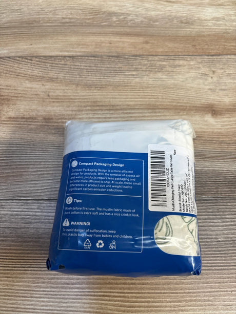 Packaged muslin changing pad cover for baby, blue label, on wood surface