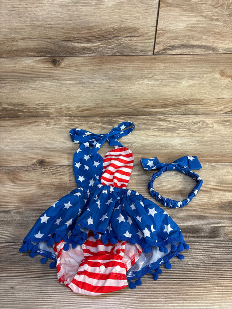 Flat lay of blue baby halter bubble romper with matching headband, stars-and-stripes print, pom-pom trim on wood background