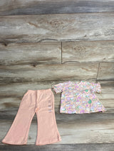 Toddlers peach bell-bottom pants with size label and pastel short-sleeve top with tennis racket pattern on wood floor