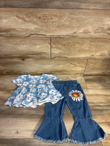 Flat-lay of girls blue daisy peplum top and denim bell-bottom pants showing ruffled hem and large daisy patch on pant leg on wood floor background