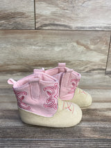 Side view of pink Stepping Stones cowgirl crib boots showcasing embroidered stitching and pull tabs on wood floor background