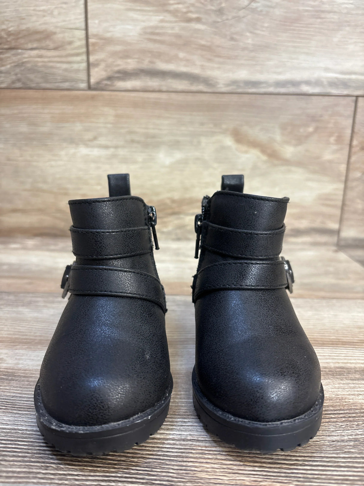 Black toddler boots with side zippers and buckle straps, kids footwear on wood floor