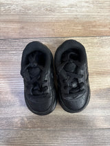Top down view of Nike Air Force 1 06 TD Triple Black toddler sneakers showcasing all black leather upper laces and perforated toe on wood plank floor