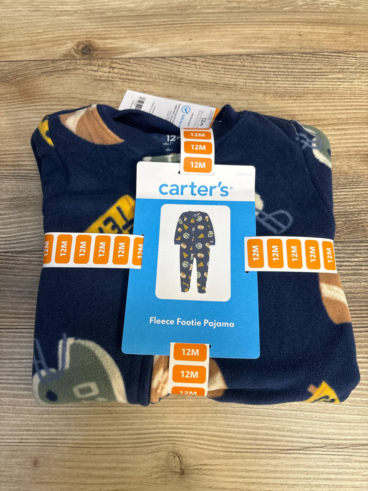 Folded Carter's fleece footie pajamas, 12 months, navy blue with sports pattern, on wood surface