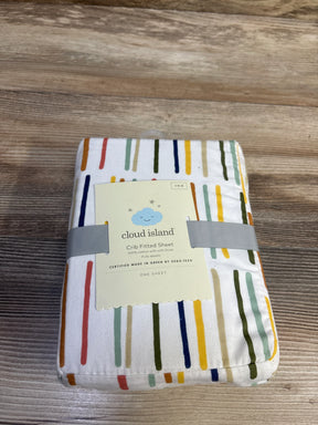 Angled top view of Cloud Island crib fitted sheet packaged, showing white with multicolor vertical dashes on wood tabletop