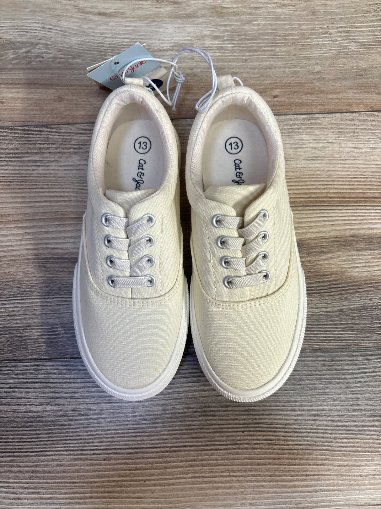 Top-down view of Cat & Jack Tyler off-white slip-on sneakers showing canvas upper and size 13 insoles on wood floor