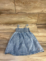 Top down view of blue toddler chambray dress with smocked bodice and knotted shoulder ties on wood floor background