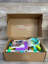 Open Lovevery Enthusiast Play Kit showing assorted toys, inner lid reads Designed by experts for child's developing brain