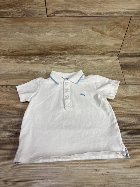 Front view of a white Tommy Bahama polo shirt with light blue collar trim, three-button placket, and embroidered logo on a wood floor