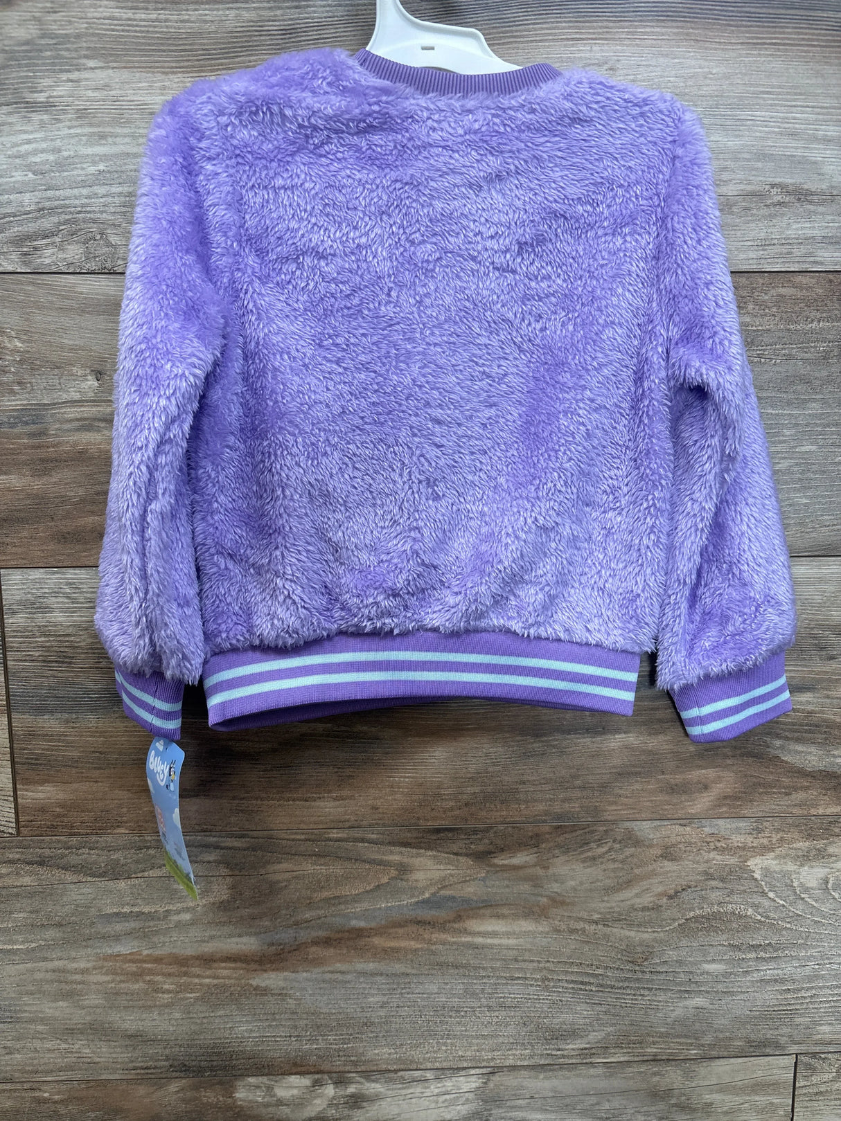 Purple fuzzy kids jacket with striped cuffs and waistband on wood background