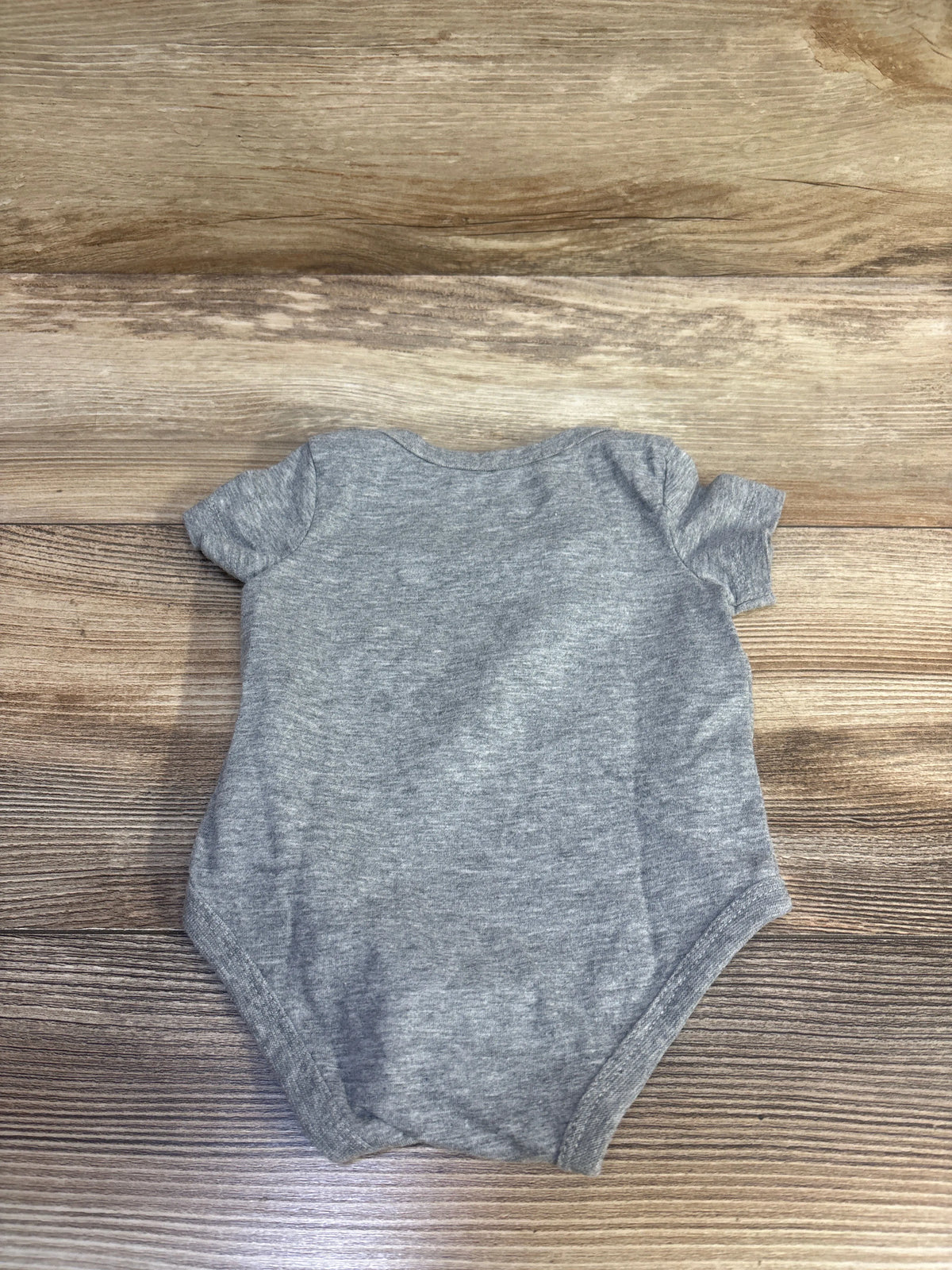 Front view of a gray Nike baby bodysuit in size 3 months showcasing short sleeves on a wood-grain surface
