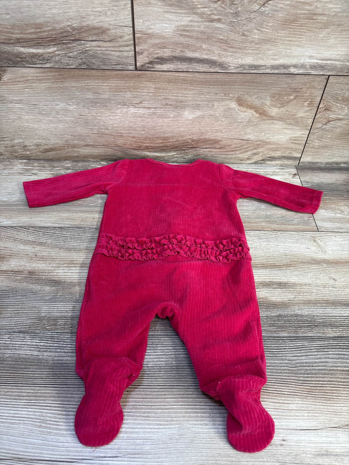 Back view of newborn red ribbed velvet sleeper with ruffle trim across back and built-in feet, laid flat on wood floor