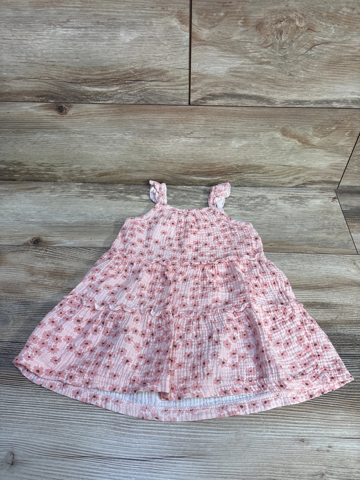 Top down view of pink floral tiered toddler dress with ruffled shoulder straps on wood plank background