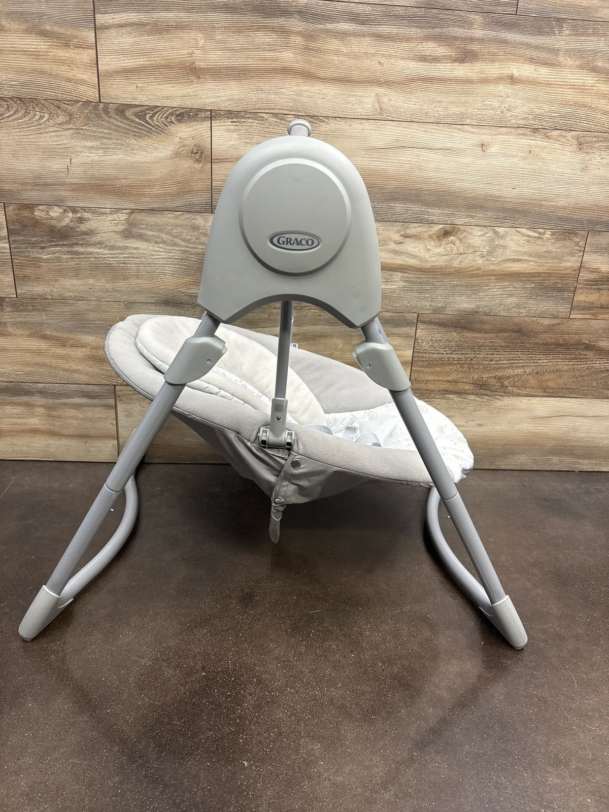 Rear view of Graco Slim Spaces Compact Baby Swing in Reign showing gray frame, padded seat, and folding legs