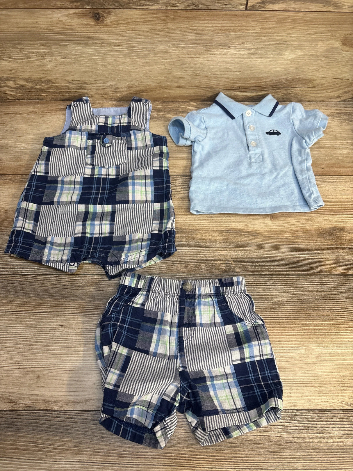 Baby boy plaid shorts, matching romper, and light blue polo shirt laid on wood floor