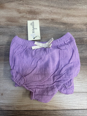 Purple baby bloomer shorts with white bow on wooden background, Vignette tag attached