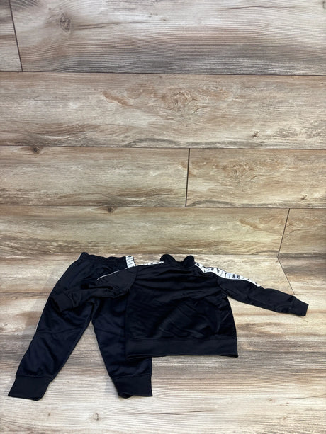 Flat lay of Nike 2-piece toddler tracksuit (18M) showing white taped logo stripe on sleeves against wood floor