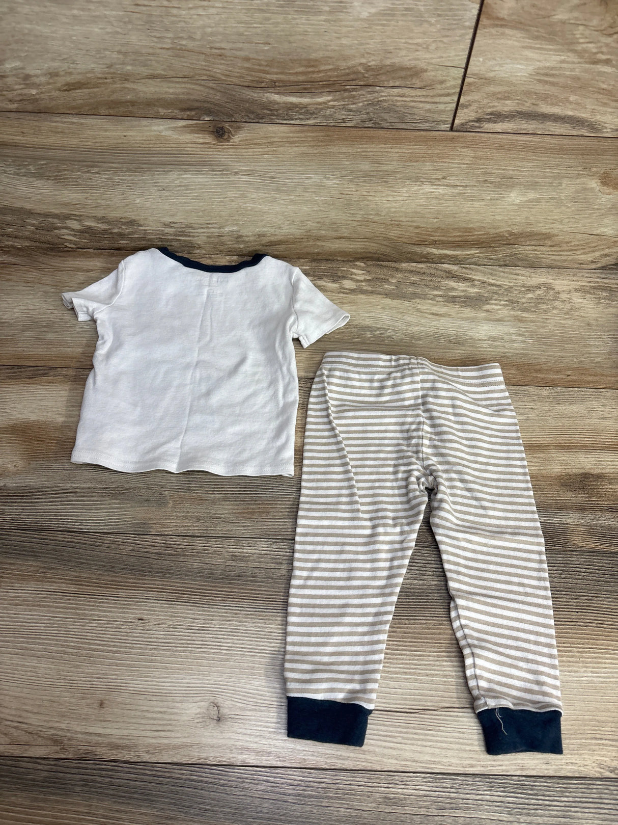White short-sleeve toddler shirt with navy collar and beige striped pants with navy cuffs on wood floor