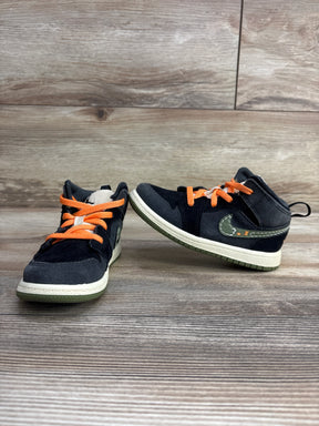 Kids black sneakers with orange laces and green accents on wood background