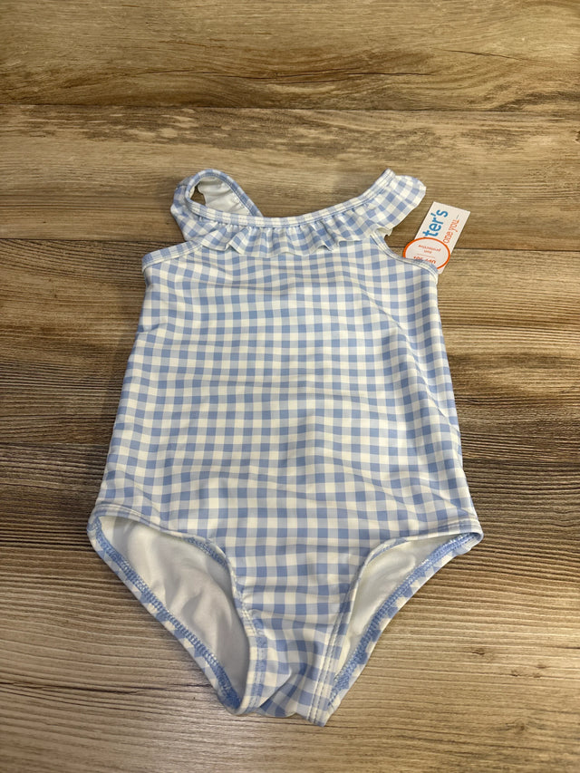 Flat lay of blue-and-white gingham toddler one-piece swimsuit showcasing ruffled one-shoulder strap and full-coverage bottom on wood background