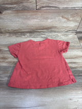 Gently used coral pink short-sleeve toddler t-shirt laid flat on wooden floor