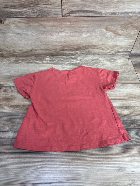 Gently used coral pink short-sleeve toddler t-shirt laid flat on wooden floor