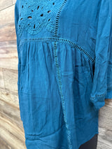 Close-up front of blue maternity lace top showing embroidered cutout bodice and ladder trim with wood background