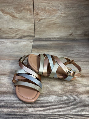 Top front view of metallic faux leather toddler sandals size 7C showing crisscross gold silver and bronze straps and buckle on wood background