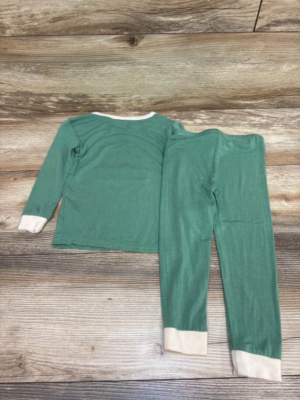 Flat lay of green two-piece bamboo pajama set with long-sleeve top, pants, and cream cuffs on a wood background