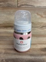 Lifefactory stainless steel baby bottle with pink protective sleeve and clear nipple cover on wooden surface
