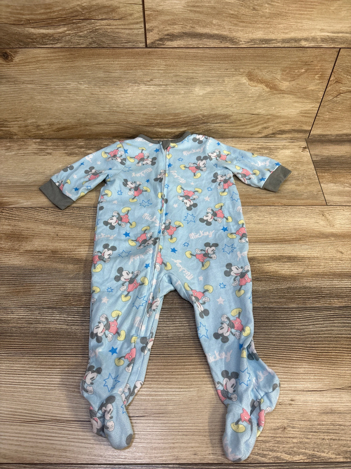 Flat lay of newborn light blue Disney Mickey Mouse footed sleeper with front zipper and grey cuffs on wood floor