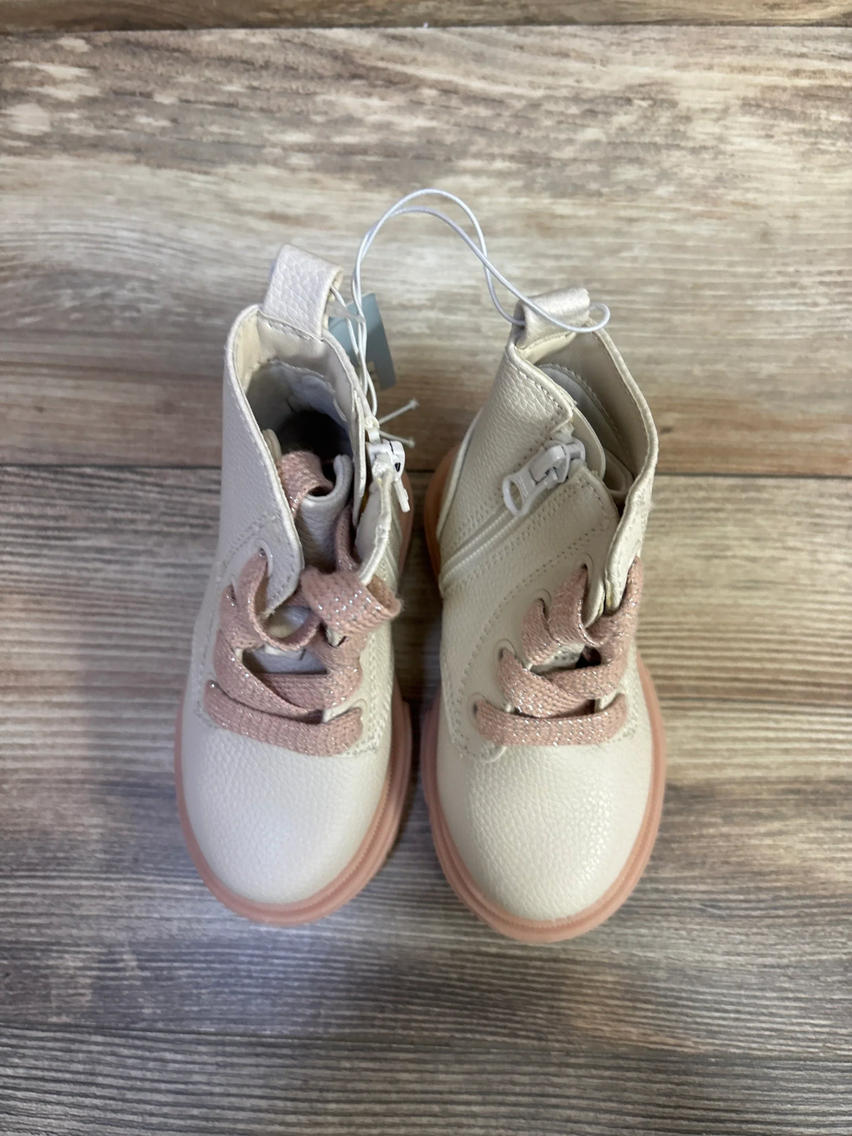 Overhead view of Amaya toddler zipper combat boots in cream and pink showing side zippers and glittery laces on wood floor