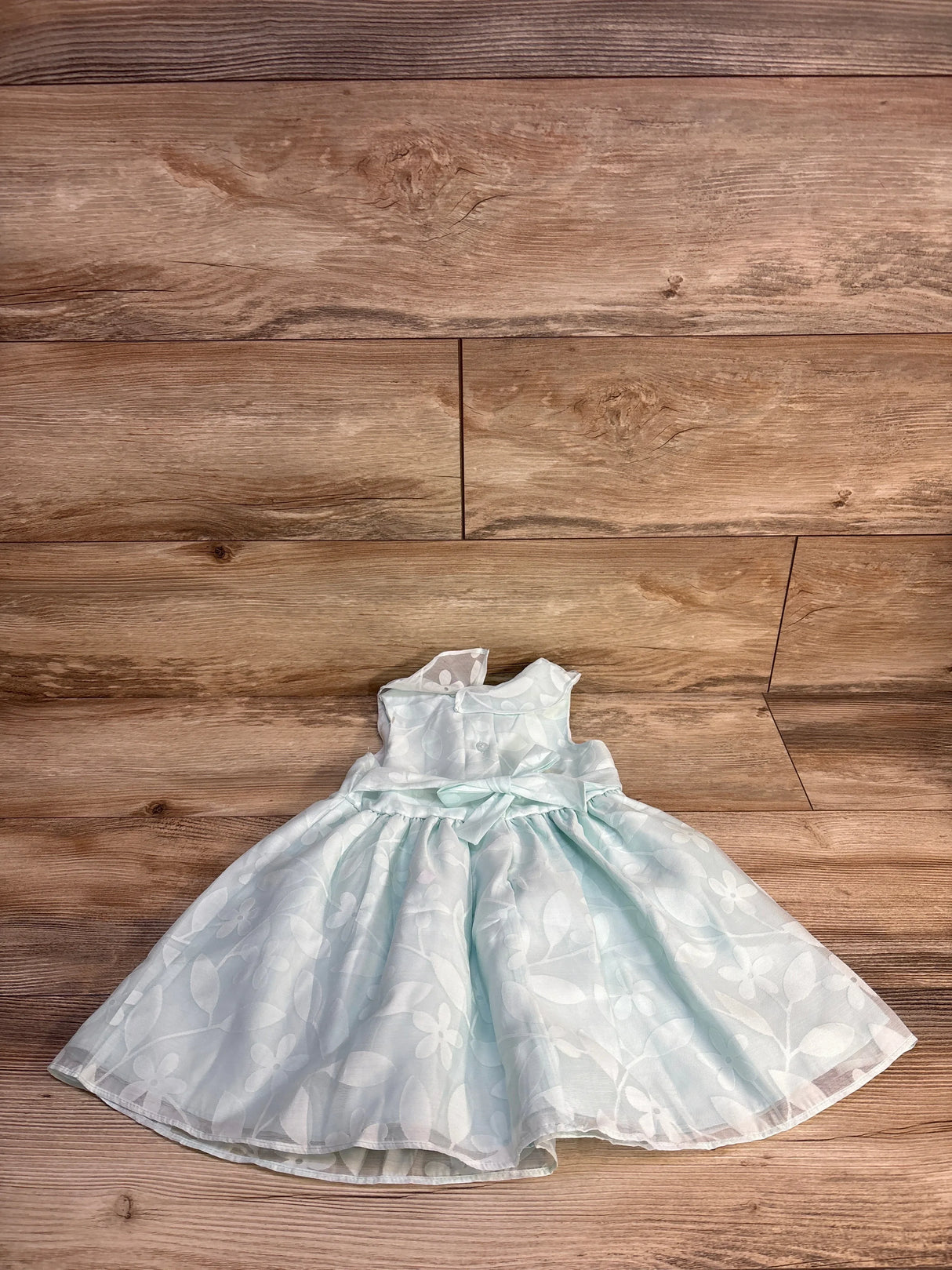 Light blue floral sleeveless girls dress with satin bow on wood background