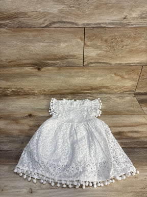White lace baby dress with pom pom trim on wooden background