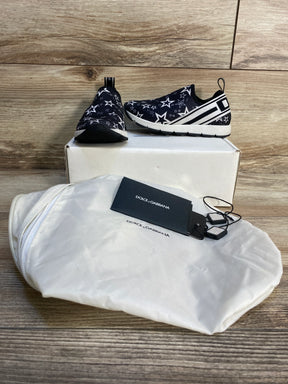 Children's black slip-on sneakers with white star pattern, dust bag, and tags displayed on wood
