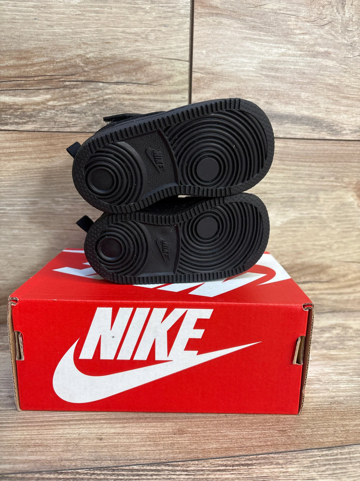 Black Nike baby sneakers on red box, ideal for kids' footwear resale