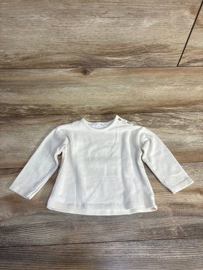 White long sleeve baby shirt with shoulder snaps, size 6-9 months, laid on wood floor