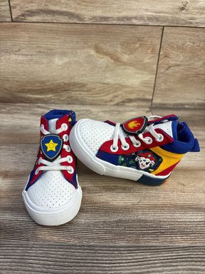 Three-quarter view of Ground Up Paw Patrol high-top sneakers size 6C with white toe, tri-color panels and character badge on wood background