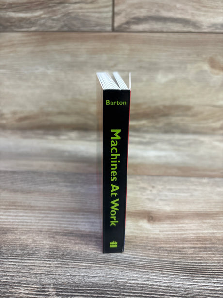 Spine view of Machines At Work board book showcasing vertical green title and author 'Barton' with wood tabletop background