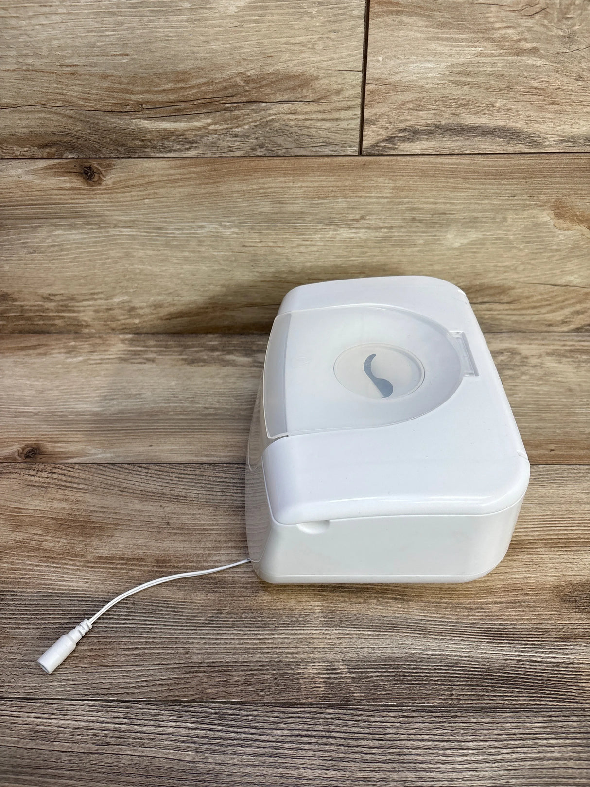 Angled view of Munchkin wipe warmer showing translucent top, circular dispenser opening, and power cord on wood surface