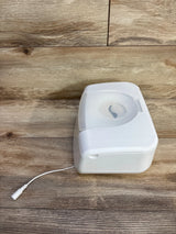 Angled view of Munchkin wipe warmer showing translucent top, circular dispenser opening, and power cord on wood surface