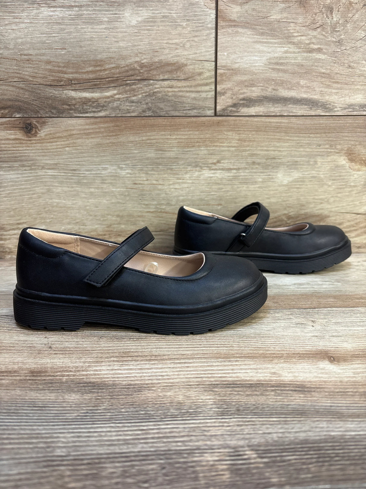 Black girls' Mary Jane dress shoes with hook-and-loop straps on wood background