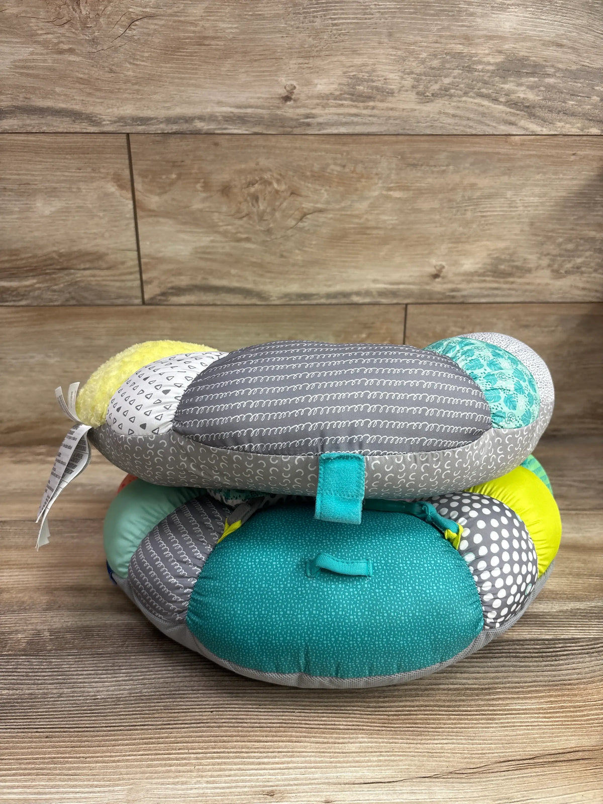 Front view of Infantino 2-in-1 Tummy Time and Seated Support showcasing multicolored patterned cushions with a wood plank background
