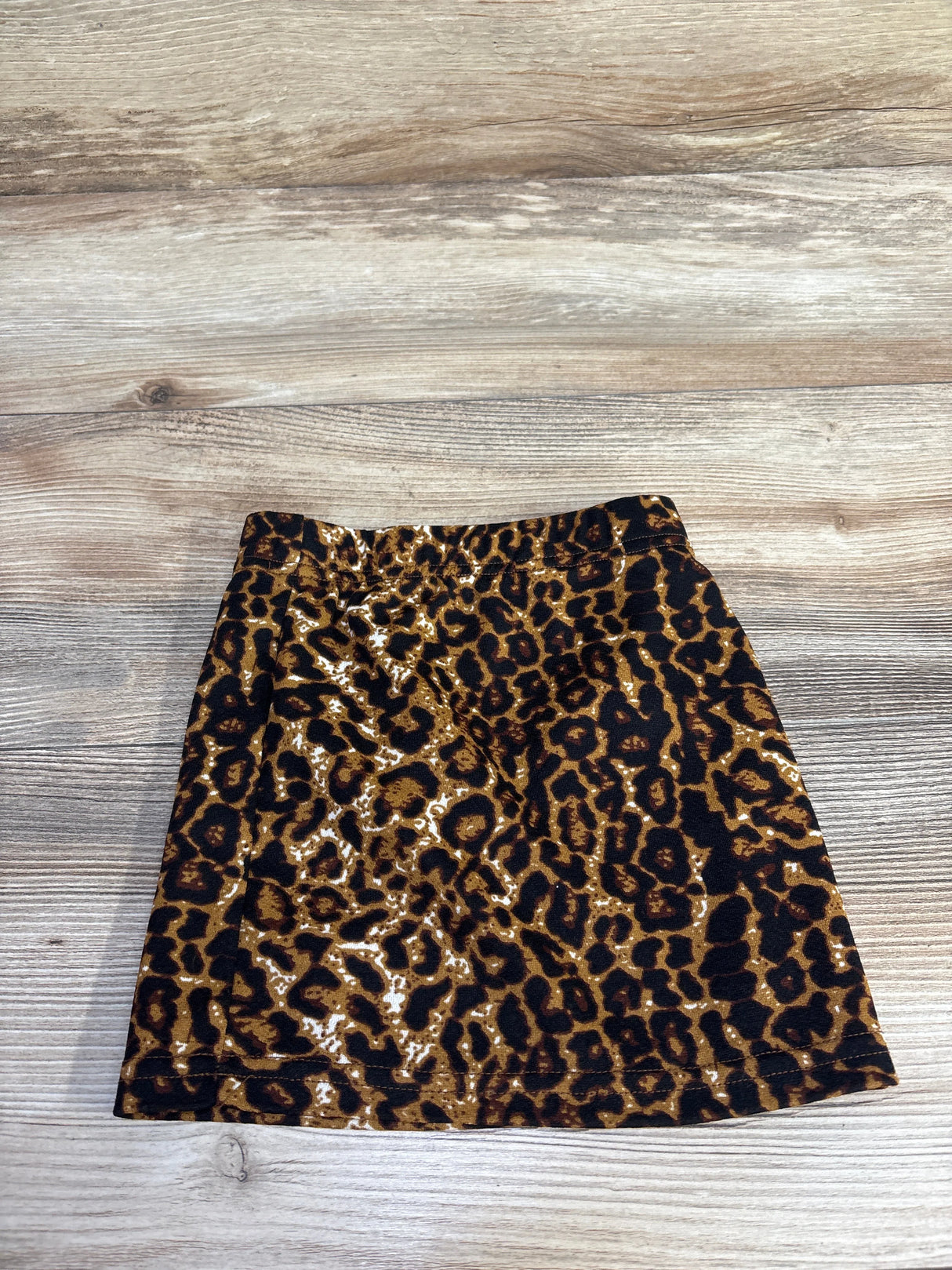 Flat lay of toddler leopard-print skirt size 2T with brown and black print and elastic waistband on light wood background