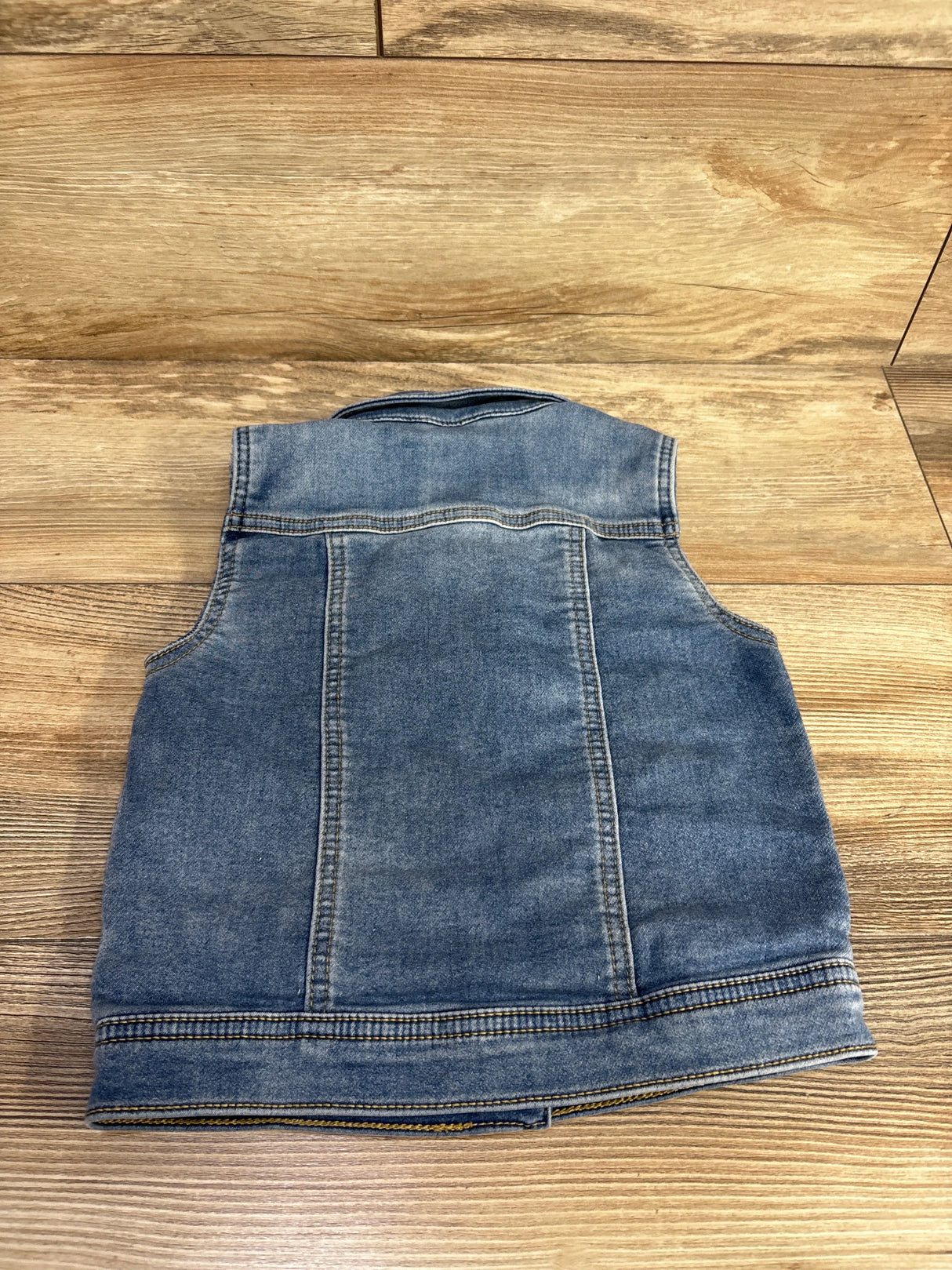 Back view of Cat & Jack denim vest size 5T showing faded blue denim panels and topstitching on wooden floor background