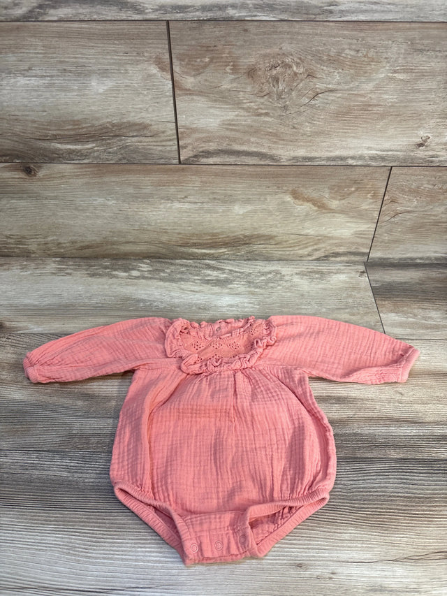 Pink baby onesie with long sleeves and ruffled neckline on wood floor