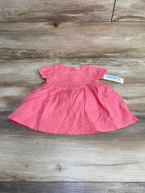 Flat lay of pink baby dress with crinkled texture, puff sleeves, gathered skirt, and Carter's tag on light wood background