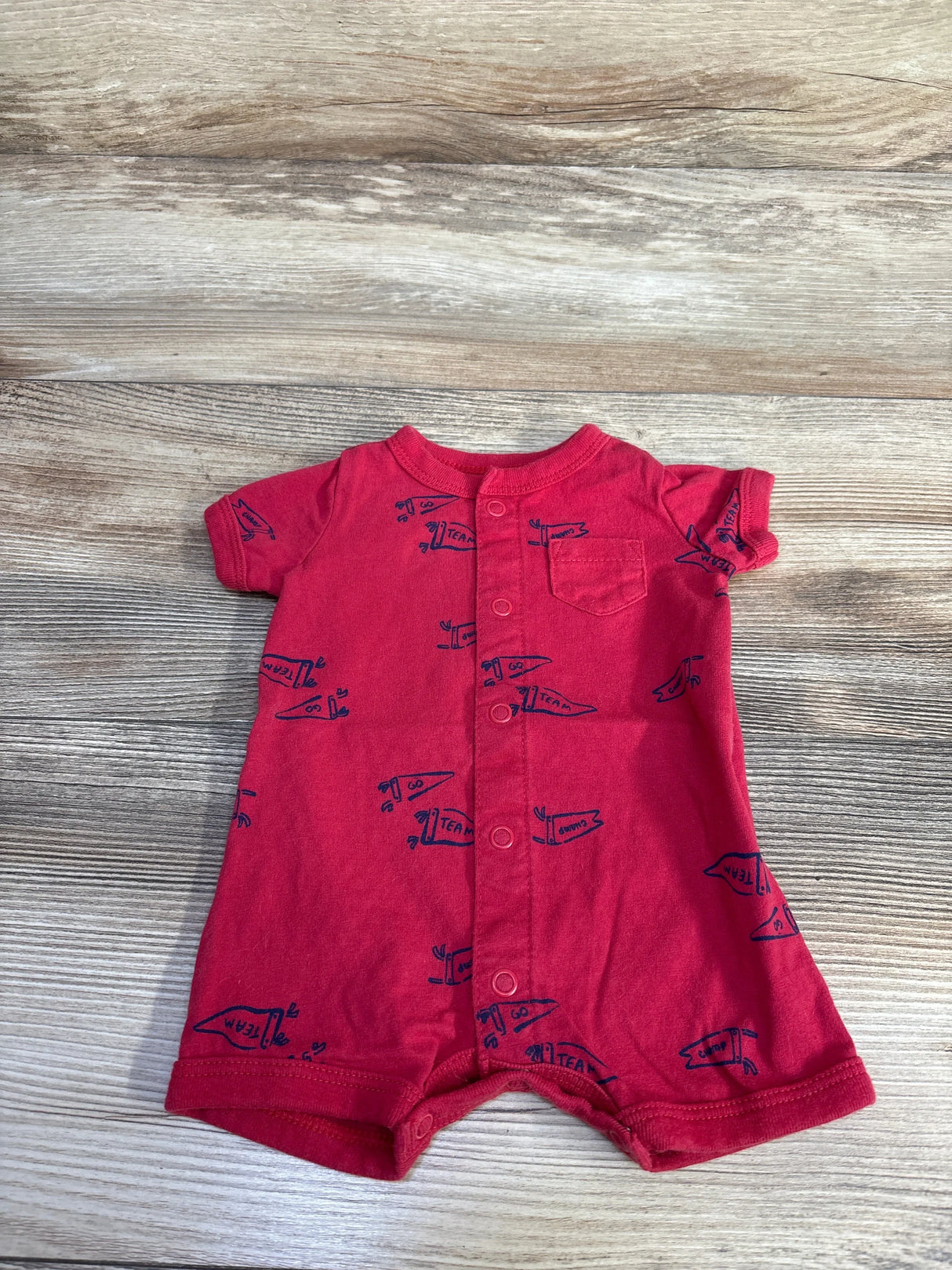 Front view of newborn red Carter's shortie romper with button-front, chest pocket, short sleeves and navy pennant print on wood